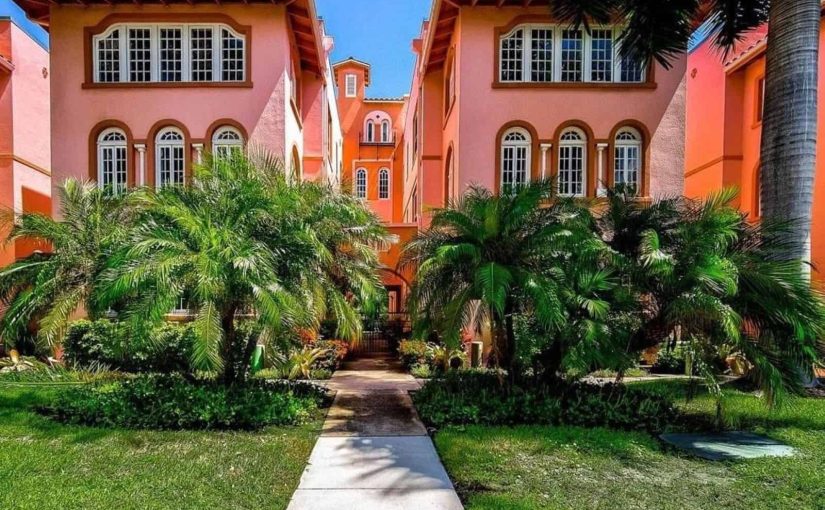 Exterior view of the historic Frances Carlton condominium in downtown Sarasota, featuring pink Mediterranean Revival architecture and lush palm trees.