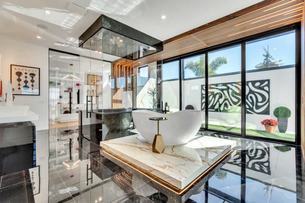 Modern bathroom with a freestanding tub, marble countertop, and floor-to-ceiling windows overlooking a garden.