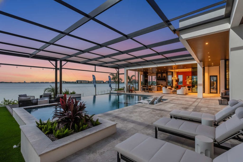 Infinity pool with lounge chairs and a modern covered patio overlooking a waterfront.